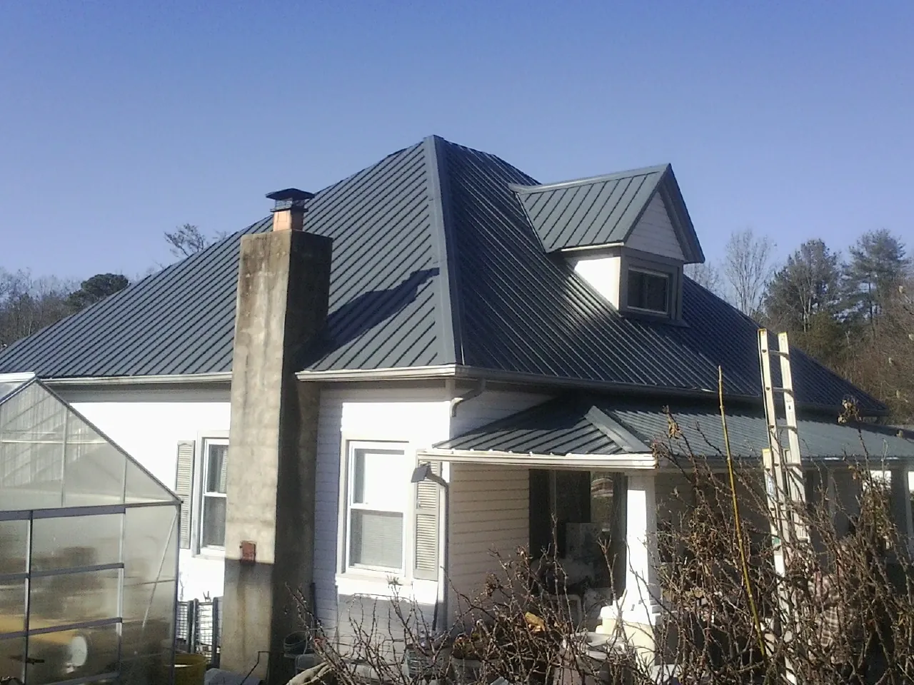 Dark blue standing seam metal roof on a white farmhouse with dormer — Slate & Tile Roof Repair by Roofing Brothers in Lynd