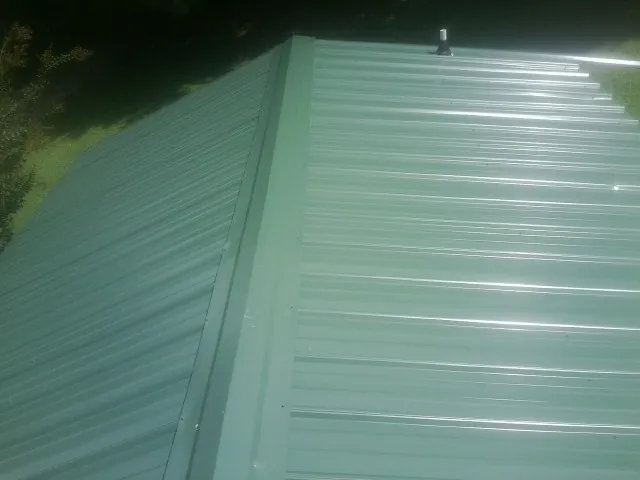 New green metal panels meeting at the ridge of a roof — Flat Roof Repair work by our crew in Lynd