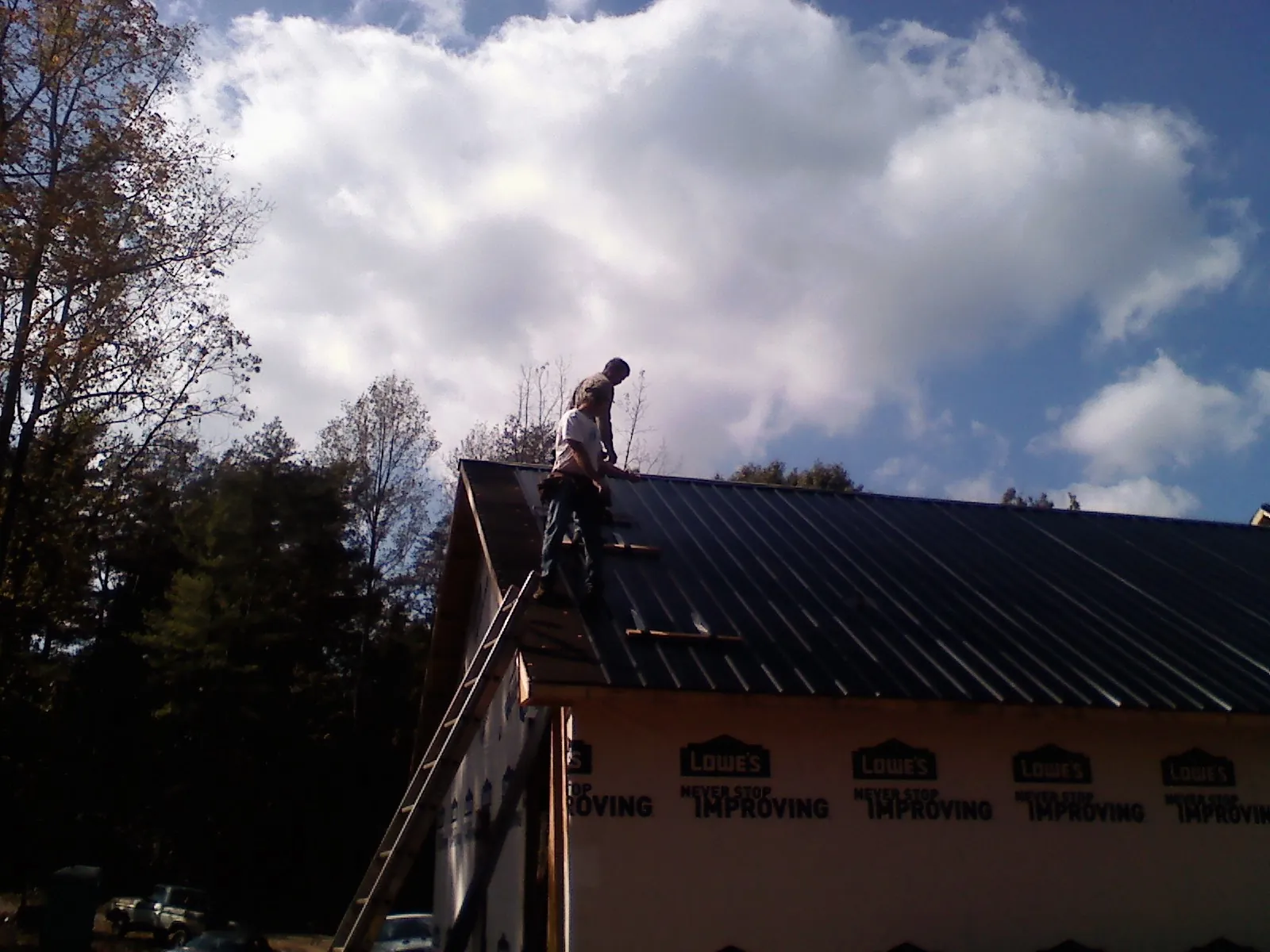 Roofer fastening dark metal panels high against a cloudy sky, from a Roof Inspection job in Lynd