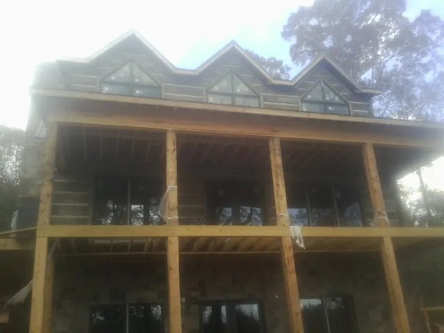 Dormers and porch framing on a large log home under construction — Roof Coating work by our crew in Lynd
